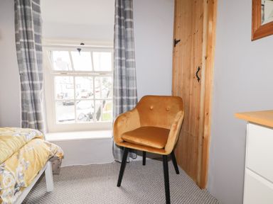 A room with a mustard-colored chair near a wooden door and a window with checkered curtains at Kooky Cottage in Brecon