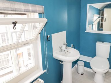 A bathroom with a white toilet a pedestal sink a window with a roller blind and a mirror on the wall at Kooky Cottage in Brecon