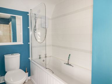 A bathroom with a toilet and a bathtub with a glass shower screen at Kooky Cottage in Brecon
