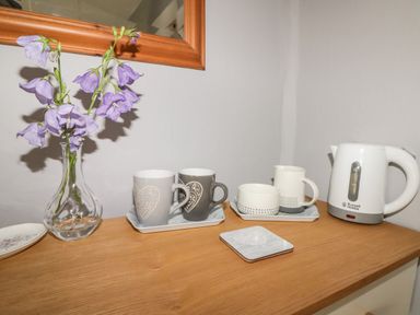 A wooden surface with a vase of purple flowers a white kettle and four mugs on trays at Kooky Cottage in Brecon