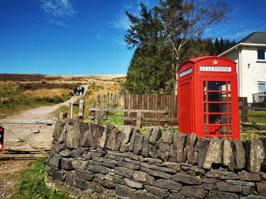 A red telephone box next to a stone wall near a dirt pathway with people walking at Kooky Cottage in Brecon