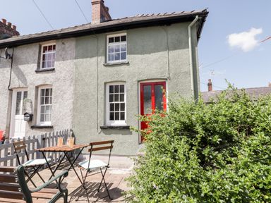 Exterior of a two-story terrace house with a red front door and a garden patio with table and chairs at Kooky Cottage in Brecon