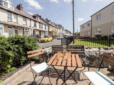 Outdoor seating area with wooden table and chairs on a paved patio by a residential street at Kooky Cottage in Brecon