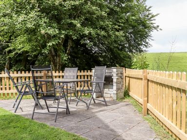 Outdoor patio area with a table and four chairs near a wooden fence and trees at Bybrook Lodge in Davidstow near Camelford