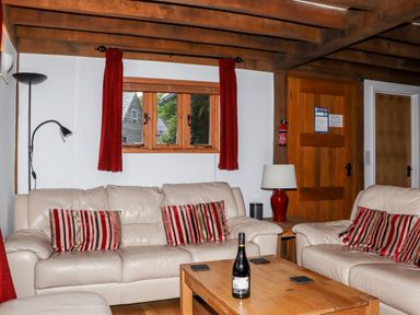 A living room with beige leather sofas red striped cushions wooden beams and a wooden coffee table with a bottle at Bybrook Lodge in Davidstow near Camelford