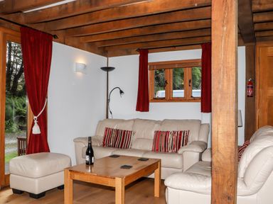 A living room with beige leather sofas red curtains wooden coffee table and a bottle at Bybrook Lodge Davidstow near Camelford