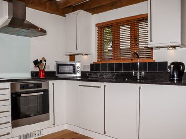 A kitchen with white cabinets a microwave stainless steel oven and a window with wooden blinds at Bybrook Lodge Davidstow near Camelford