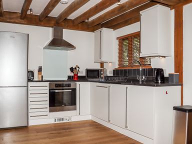 A kitchen with white cabinets wooden beams a refrigerator oven microwave and sink at Bybrook Lodge in Davidstow near Camelford