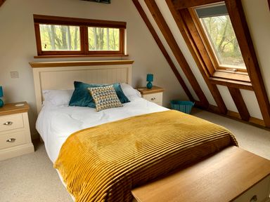 A bedroom with a double bed with white bedding and yellow blanket two bedside tables with lamps and wooden beams on the ceiling at Bybrook Lodge in Davidstow near Camelford
