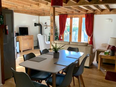 A dining area with a table and six chairs next to a living room with sofas and a television at Bybrook Lodge in Davidstow near Camelford