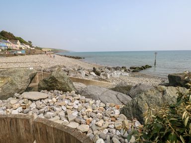 A pebble beach with large rocks and a sea marker with houses in the background at The Dingle in Wisemans Bridge near Stepaside