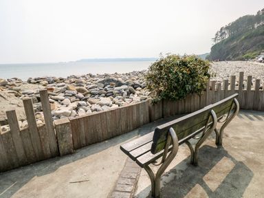 A bench overlooking a rocky beach with wooden fencing and bushes at The Dingle in Wisemans Bridge near Stepaside
