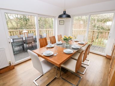 A dining room with a set table and wooden chairs next to large sliding glass doors at The Dingle in Wisemans Bridge near Stepaside