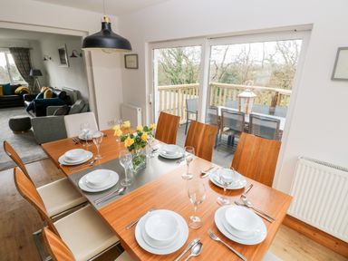 A dining area with a wooden table set for six and sliding glass doors leading to an outdoor deck at The Dingle Wisemans Bridge near Stepaside