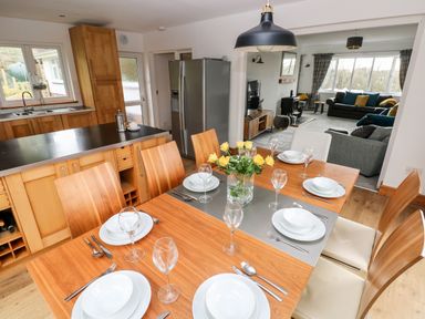 A dining table set with plates glasses and cutlery next to a kitchen with wooden cabinets and a refrigerator at The Dingle Wisemans Bridge near Stepaside