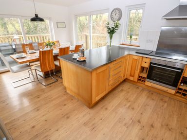 A kitchen and dining area with wooden cabinets black countertops and a dining table set with plates glasses and flowers at The Dingle in Wisemans Bridge near Stepaside