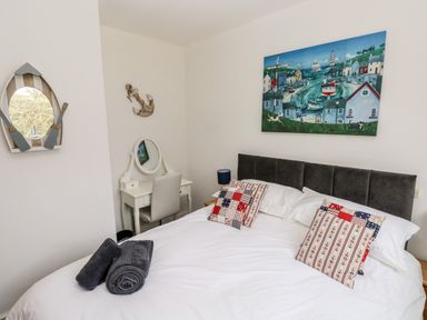 A bedroom with a double bed with patterned cushions a vanity desk with a chair and nautical themed wall decorations at The Dingle in Wisemans Bridge near Stepaside