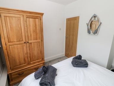 A bedroom with a wooden wardrobe a wooden door and a bed with folded towels and a boat-shaped mirror on the wall at The Dingle in Wisemans Bridge near Stepaside