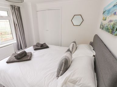 A bedroom with a bed with gray headboard white bedding gray towels and striped pillows a window with gray curtains and a closet door a hexagon mirror and a beach painting on the wall at The Dingle Wisemans Bridge near Stepaside