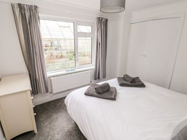 A bedroom with a bed and folded towels on it a chest of drawers a window with curtains and a built-in wardrobe at The Dingle Wisemans Bridge near Stepaside