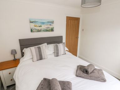 A bedroom with a double bed with pillows and towels a bedside table with a lamp and a door on the wall at The Dingle in Wisemans Bridge near Stepaside