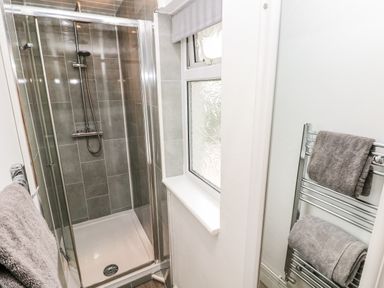A bathroom with a glass enclosed shower with gray tiles a window and a heated towel rail with gray towels at The Dingle in Wisemans Bridge near Stepaside