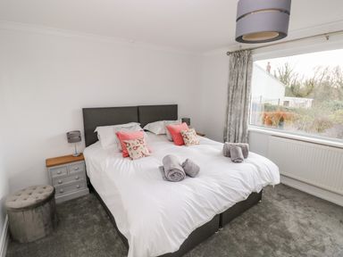 A bedroom with a double bed two bedside tables lamps and a large window with curtains at The Dingle in Wisemans Bridge near Stepaside