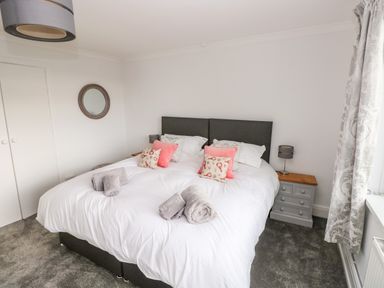 A bedroom with a double bed white bedding pink and patterned cushions bedside tables lamps a round wall mirror and patterned curtains at The Dingle in Wisemans Bridge near Stepaside