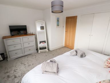 A bedroom with a bed, folded towels, a gray dresser with a TV, a full-length mirror, a wooden door, and white closet doors at The Dingle in Wisemans Bridge near Stepaside