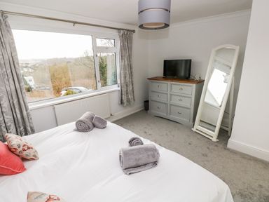 A bedroom with a bed and towels on it a dresser with a television and a standing mirror by the wall at The Dingle in Wisemans Bridge near Stepaside