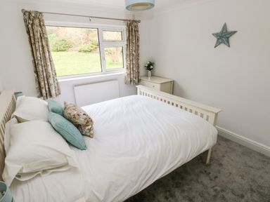 A bedroom with a bed, a window with curtains, a cabinet with flowers, and a star decoration on the wall at The Dingle in Wisemans Bridge near Stepaside