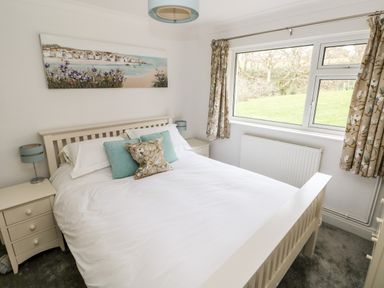 A bedroom with a bed white bedding two bedside tables with lamps and a window with floral curtains at The Dingle in Wisemans Bridge near Stepaside