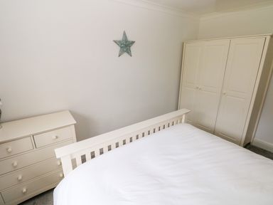 A bedroom with a white bed frame white dresser and white wardrobe with a star decoration on the wall at The Dingle in Wisemans Bridge near Stepaside