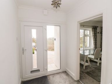 An entrance hallway with a white front door and glass side panel next to a room with a glass desk and white chair at The Dingle in Wisemans Bridge near Stepaside