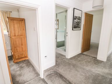 A hallway with open doors leading to a room with a wardrobe a bathroom with a shower and another room at The Dingle in Wisemans Bridge near Stepaside