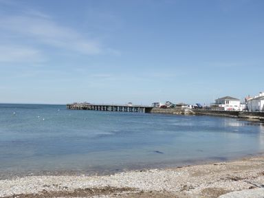 A view of a pier extending into the sea with buildings and boats near the shore at Still Waters in Swanage