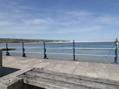 A wooden bench and metal railing overlooking a body of water with hills in the background at Still Waters in Swanage