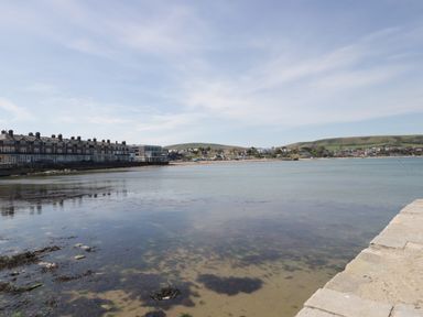 A coastal view with buildings along the shore and hills in the background at Still Waters in Swanage