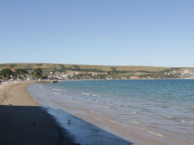 A sandy beach with small waves and a coastal town with hills in the background at Still Waters in Swanage