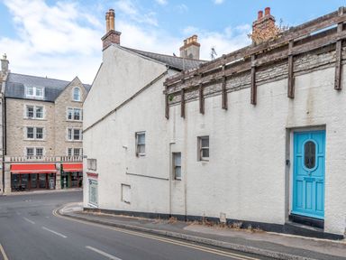 A street corner with a white building with small windows and a blue door next to a road with a building with red awnings across the street at Still Waters in Swanage