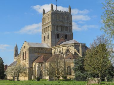 An old stone church building with a large tower and surrounding trees and grass under a blue sky at Runnymede in Tewkesbury