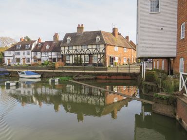 A riverside view showing historic timber framed and brick houses with boats on water at Runnymede in Tewkesbury