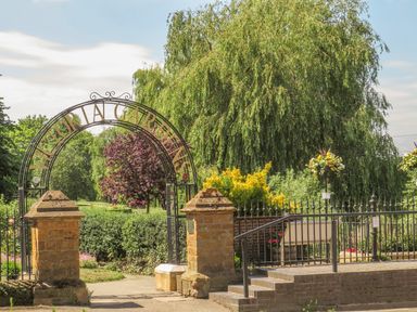 A garden entrance with an iron arch reading Victoria Gardens and greenery in the background at Runnymede in Tewkesbury