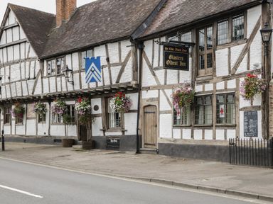 A street view of a timber framed building with hanging flower baskets and a sign for Glosters Oldest Inn at Runnymede in Tewkesbury