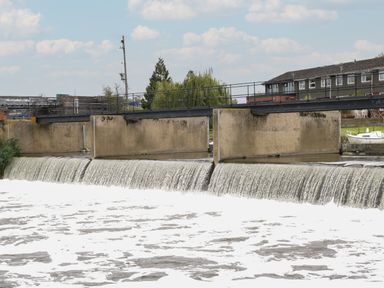 A concrete weir with water flowing over it and a metal railing above at Runnymede in Tewkesbury