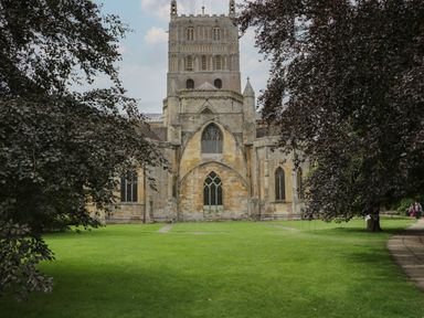 A large stone church building with stained glass windows surrounded by grass and trees at Runnymede in Tewkesbury