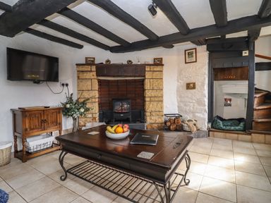 A living room with a wooden coffee table a stone fireplace a wall-mounted tv and wooden stairs at Runnymede in Tewkesbury