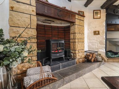 A fireplace with a wood-burning stove surrounded by stone and brick with blankets in a basket and a wood basket at Runnymede in Tewkesbury