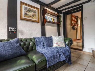 A green leather sofa with blue cushions and a blanket in a room with white textured walls and black ceiling beams at Runnymede in Tewkesbury