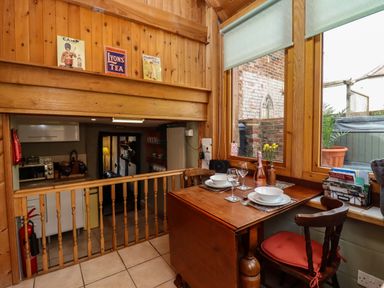 A small dining area with a wooden table set for two next to large windows overlooking a brick wall at Runnymede in Tewkesbury